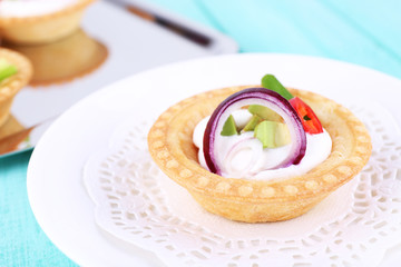 Tartlet with greens and vegetables with sauce on plate on table