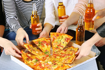 Friends hands with bottles of beer and pizza, close up