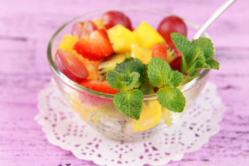 Fruit salad with mint in glassware on color wooden background