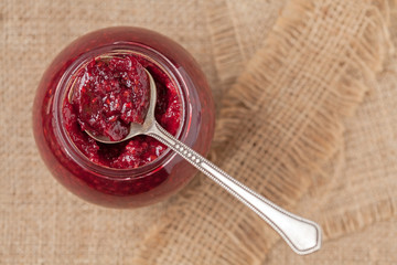 Jar of berry jam with spoon on vintage textile background. Top v