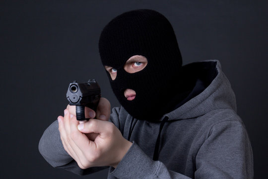 man criminal in black mask aiming with gun over grey