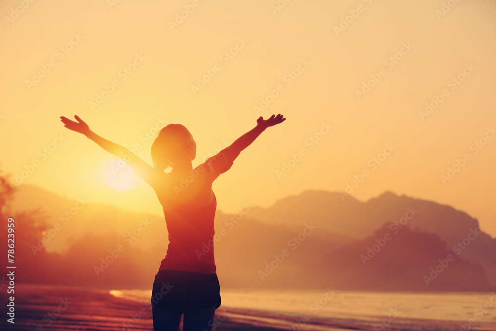 Wall mural cheering woman hiker open arms at sunrise seaside beach 