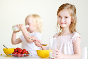 Two cute little sisters eating cereal in a kitchen