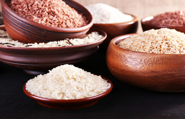 Different kinds of rice in bowls on wooden background