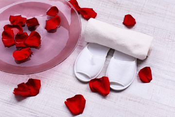 Spa bowl with water, rose petals, towel and slippers