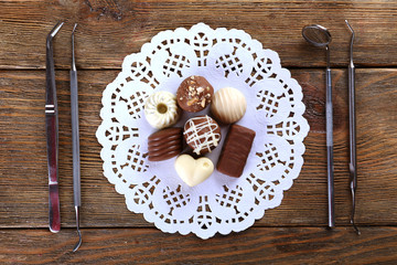 Dentist tools with sweets on lacy napkin on wooden background