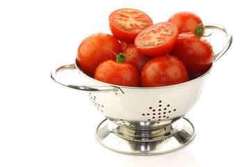 fresh  tomatoes and a cut one in a metal colander