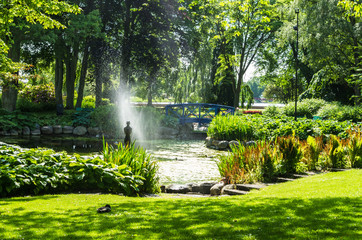 Fototapeta na wymiar Park with water fountain and a statue in a pond.