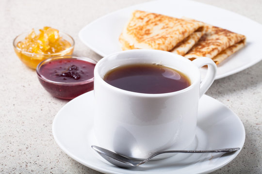 Cup of tea with two kinds of jam and russian pancakes - blini