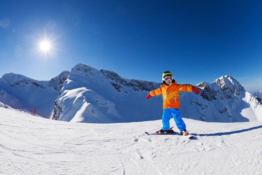 Happy boy in ski mask with arms apart skiing alone