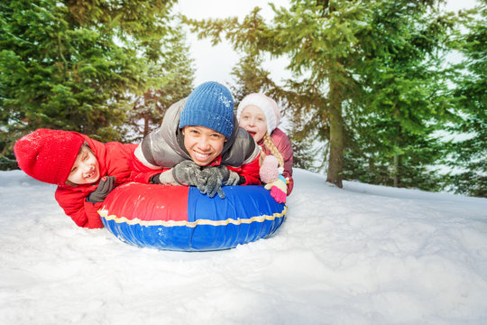 Excited girl and two boys on snow tube in winter