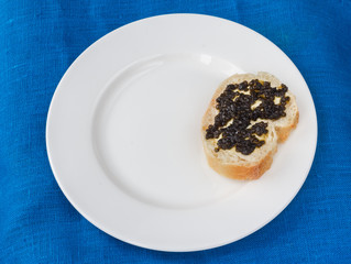 One sandwich with black caviar on white plate. Top view