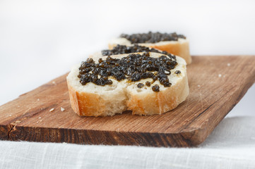 Sandwiches with black caviar lying in a row on a wooden surface