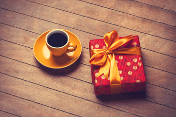 Cup of coffee and gift box on a wooden table.