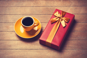 Cup of coffee and gift box on a wooden table.