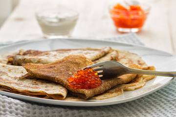 plate with pancakes and red caviar on a wooden table
