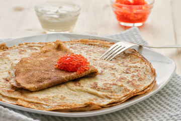 Baked pancakes with red caviar on a plate on a wooden table 