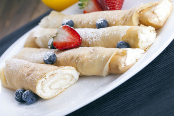 Delicious sweet rolled pancakes on a plate with fresh fruits