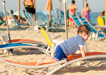 Sweet toddler dressed as a sailor crawling on a sunbed on a beac