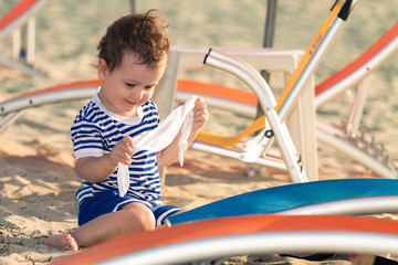 Toddler dressed as a sailor playing with his clothes near sunbed