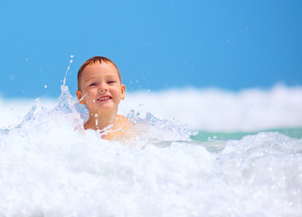 Fototapeta na wymiar cute excited boy having fun in waves, summer vacation
