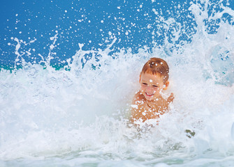 cute excited boy having fun in waves, summer vacation