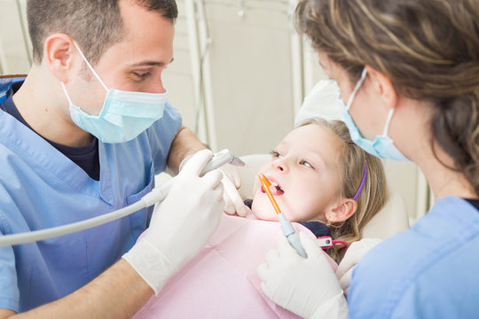 Dentist and dental assistant examining young girl teeth