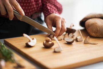 Fototapeta na wymiar Closeup on young housewife cutting mushrooms in kitchen