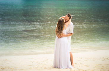 Fototapeta na wymiar blonde bride and groom kiss standing at sand beach