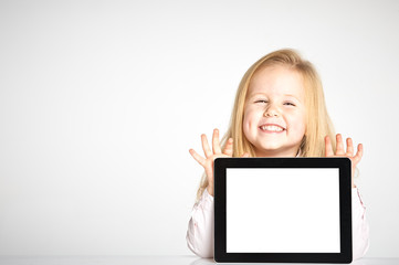 Cute little and smiling girl plays with a tablet