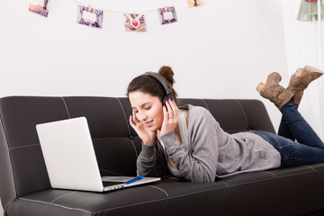 Beautiful young woman using laptop and listening music at home