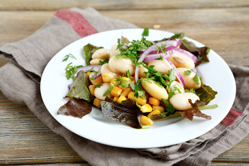 Tasty salad with beans, lettuce, onions and corn on a plate