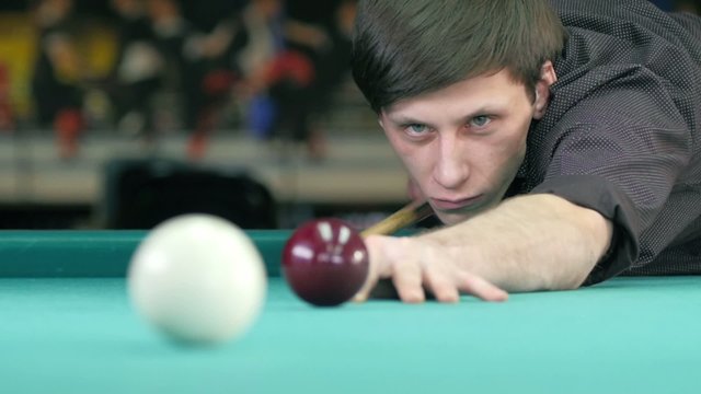 Guy takes aim, to make an impact on a billiard ball. Slow motion