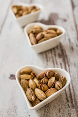 Pistachio Nuts in Heart Shaped Bowls on White Wooden Bacckground
