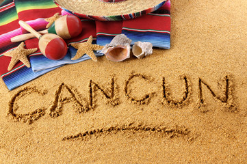 Cancun beach writing word written in sand on a mexico beach with sombrero and traditional blanket photo