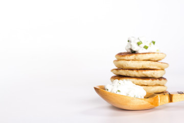 isolated several pancake and wooden spoon with sour cream and he