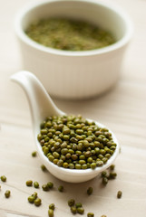 Raw mung beans in ceramic spoon over white wooden background