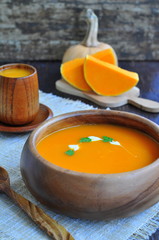 Vegetarian pumpkin soup in dark wooden bowl on a wooden table
