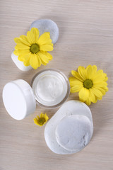 Cosmetic cream with flowers and spa stones on wooden background