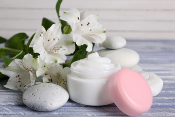 Cosmetic cream with flowers and spa stones on wooden background