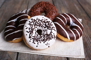 Delicious donuts with icing on napkin on wooden background