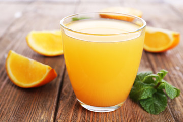 Glass of orange juice with oranges on wooden table close up