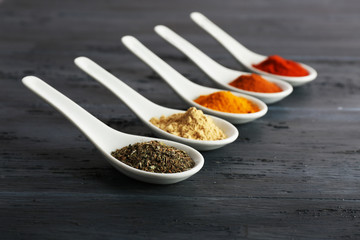 Different kinds of spices in spoons on wooden background