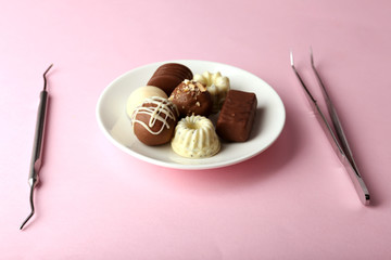 Dentist tools with sweets on plate on pink background