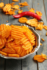 Delicious potato chips on plate on wooden table close-up