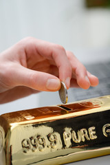 hand droping a coin in gold ingot shaped piggy bank money box