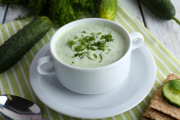 Cucumber soup in bowl on color wooden table background