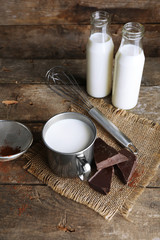 Metal mug and glass bottles of milk with chocolate chunks and