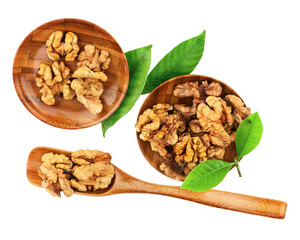 Handful of walnuts in wooden bowls, scoop and green leaves.