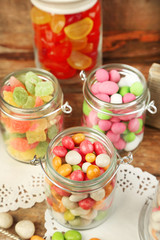 Multicolor candies in glass jars on wooden background